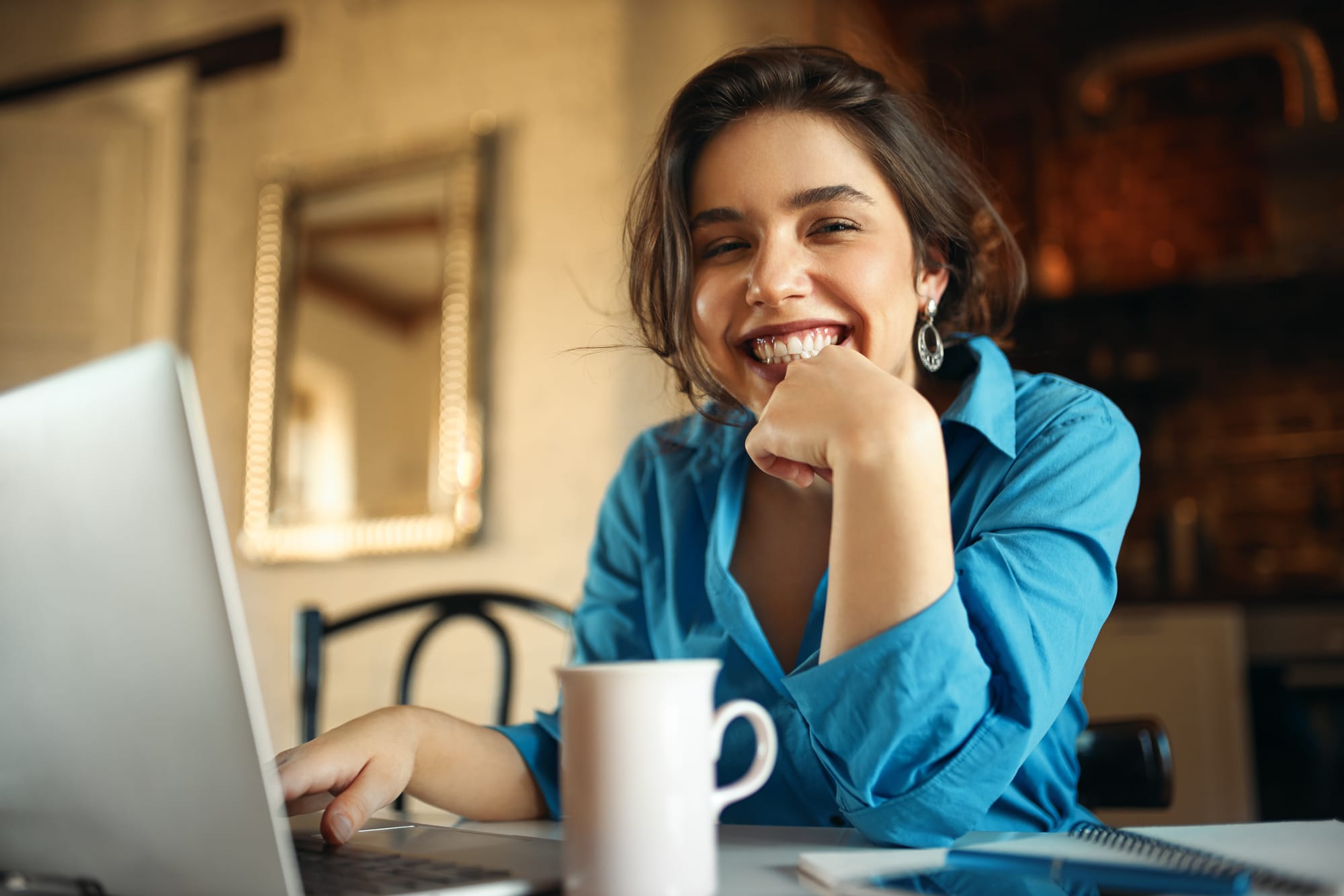 mulher-jovem-e-atraente-alegre-apreciando-um-trabalho-distante-sentado-na-mesa-usando-um-computador-portatil-bebendo-cafe-blogueira-bonita-trabalhando-em-casa-enviando-video-em-seu-canal-sorrindo